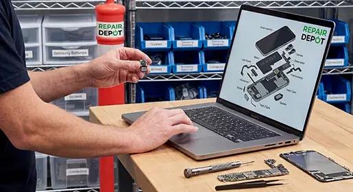 Person checking a laptop holding a camera in a workshop with tools and parts on a table.