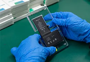 Person wearing blue gloves holding a REPART battery replacement on a green surface